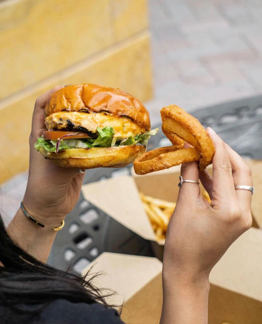 Two hands holding a burger with onion rings
